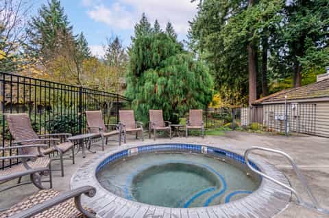 Hot tub on terrace surrounded by lounge chairs, tall trees, and forest setting