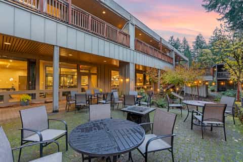 Modern resort patio at dusk with fire pit tables, lounge chairs, and illuminated building