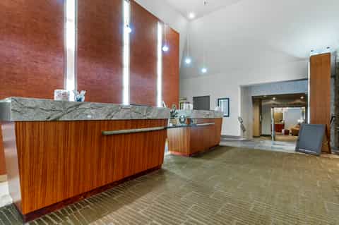 Hotel reception desk with warm wood finishes, marble countertop, and modern lighting fixtures.