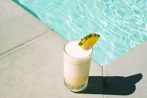 Tropical pineapple cocktail garnish at pool's edge with turquoise water