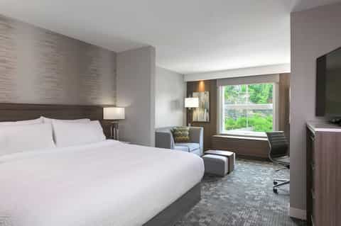 Contemporary hotel bedroom with queen bed, workspace, and scenic window view