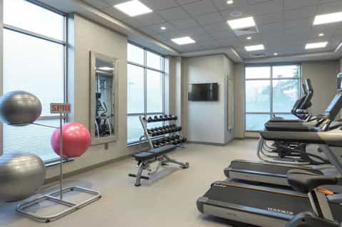 Compact hotel gym with exercise bikes, treadmills, dumbbells, and fitness balls