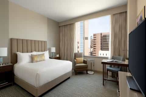 Modern hotel room with beige headboard, city skyline view, and contemporary furnishings