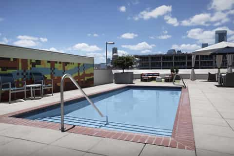 Rooftop pool deck with blue swimming pool, colorful mosaic art wall, and urban city skyline views