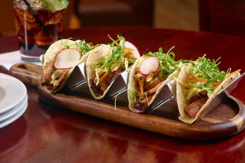 Gourmet tacos with radish, greens, and protein on wooden serving board