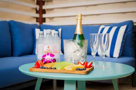 Luxury seating area with champagne bottle, water, fruit platter, and blue striped cushions overlooking water