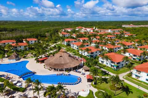 Aerial resort view with blue pools, thatched-roof common areas, and white villas in jungle setting