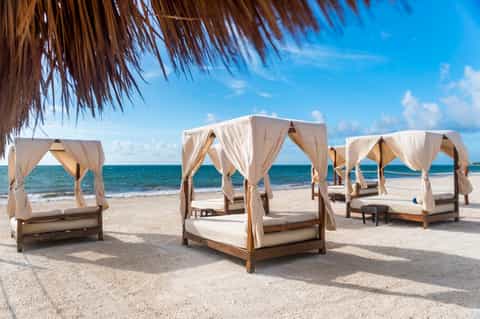 Beach cabanas with cream canopies and wooden frames on sandy shore
