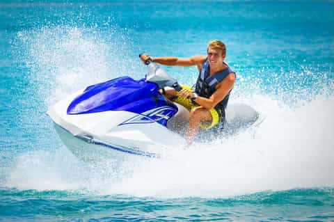 Person riding jet ski on turquoise tropical water with ocean spray
