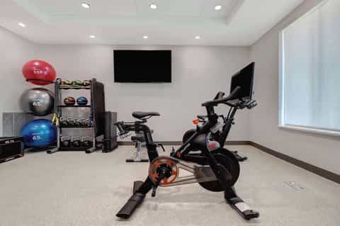 Hotel fitness center with exercise bike, stability balls, free weights, TV screen, and modern equipment rack