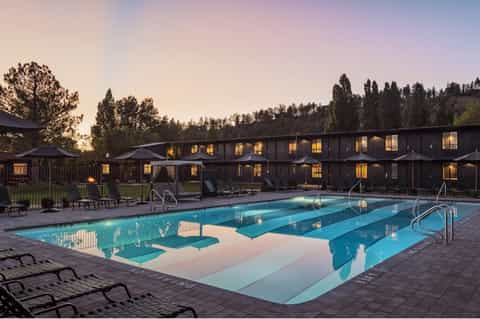 Lap pool at dusk with illuminated cabins and forested mountains in background