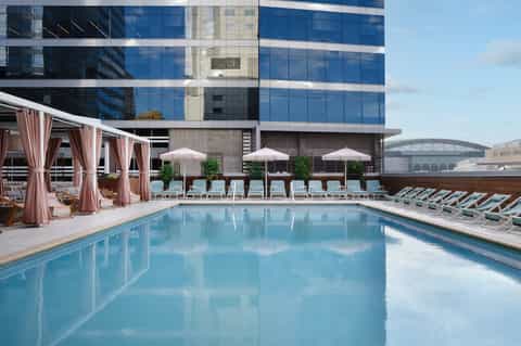 Rooftop infinity pool with city skyline views, pink cabanas, and lounge seating