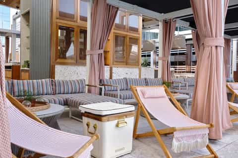 Elegant poolside lounge with striped chaises, wooden furnishings, pink curtains, and seating