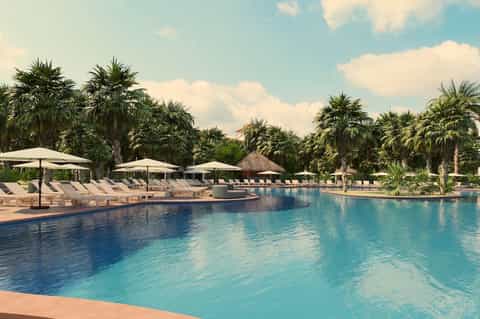 Resort pool surrounded by palm trees, white umbrellas, lounge chairs, and clear blue water