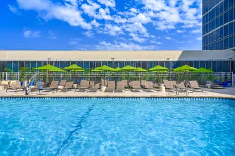Hotel outdoor pool with bright blue water, lime green umbrellas, lounge chairs, and high-rise building.