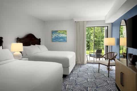 Hotel guest room with two beds, blue accent wall, balcony access, elegant furnishings, and modern decor