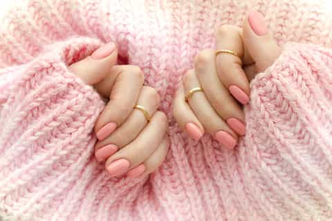 Close-up of two hands with manicured nails and gold rings on pink knit fabric