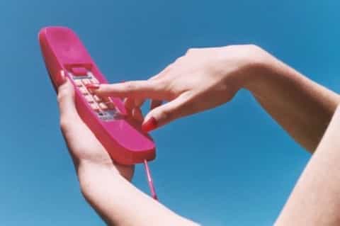 Hands holding a vintage pink rotary telephone against a blue sky background