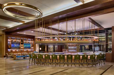 Upscale bar with circular brass lighting, glass railings, green bar stools, and premium liquor displays