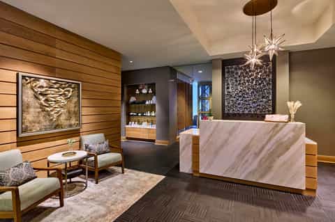 Modern hotel reception area with marble counter, wood paneling, and contemporary chandelier