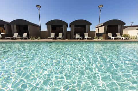 Resort pool with crystal-clear turquoise water and four dome-shaped cabanas with loungers under sunny blue sky