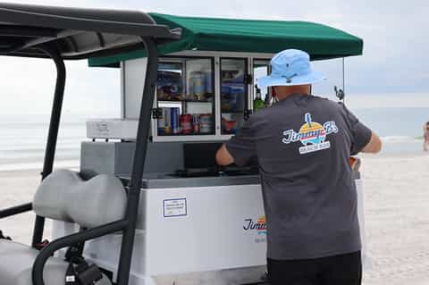 Beach bar attendant at Jimmp's Beach Bar kiosk with green canopy on sandy beach near ocean