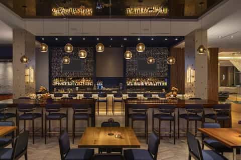 Hotel bar lounge with gold pendant lighting, dark wood accents, patterned wall panels, and modern seating