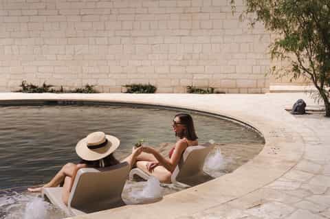 Couple enjoying shallow pool with curved stone edge and beige brick wall backdrop.
