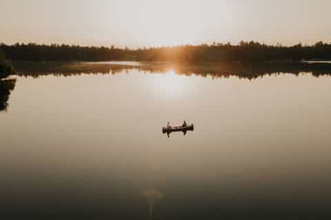 Two people in canoe on mirror-still lake at golden hour sunrise