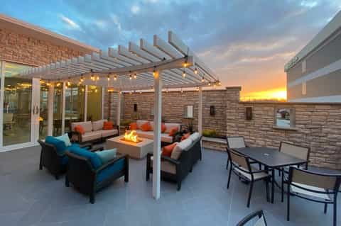 Modern patio with pergola, fire pit, colorful seating, and sunset views at dusk