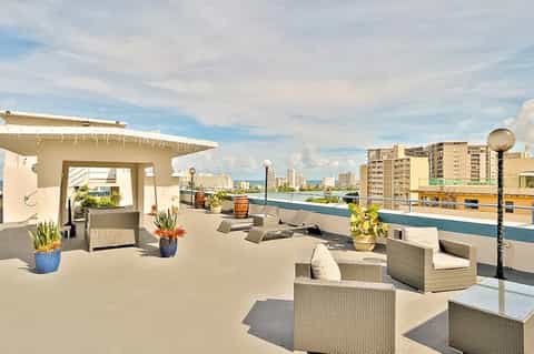 Rooftop terrace with rattan furniture, water views, modern pergola, and urban skyline in the background