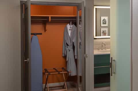 Luxury hotel closet with orange accent wall, robes, and ensuite bathroom visible