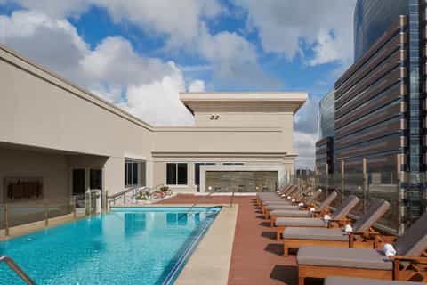 Rooftop pool deck with lounge chairs, ocean city skyline views, and modern architecture