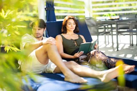 Couple relaxing on blue lounge chairs reading outdoors surrounded by lush green foliage