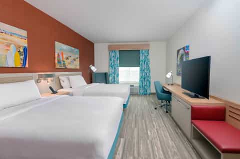 Hotel guest room with two queen beds, orange accent wall, and beachy decor