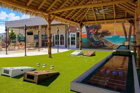 Recreational outdoor area with cornhole games, shuffleboard, and tropical bar setup