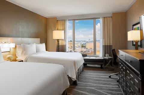 Hotel bedroom with two queen beds, warm tones, city views from large windows