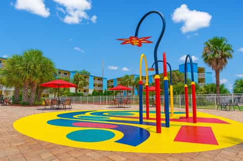 Colorful splash pad with yellow and blue play surface, rainbow arch, and red umbrella