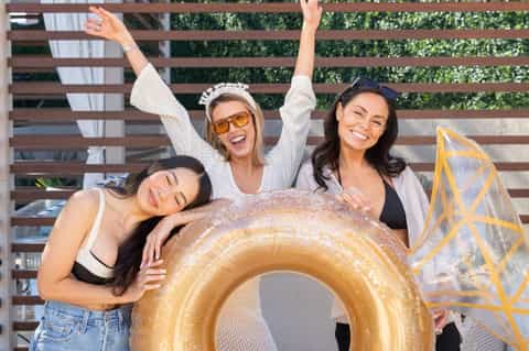 Three women posing with gold inflatable ring float at poolside lounge area