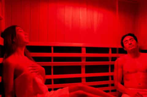 Red infrared sauna room with two people relaxing on wooden benches
