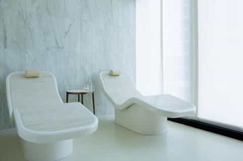 Minimalist spa relaxation area with two white curved loungers and marble walls