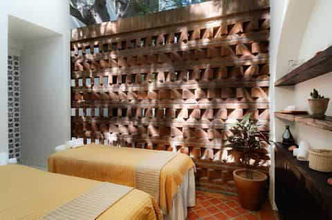 Spa treatment room with twin massage beds and geometric carved wood wall featuring sunlight patterns.