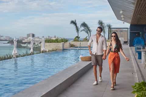 Couple walking along an infinity pool edge with waterfront city views and palm trees