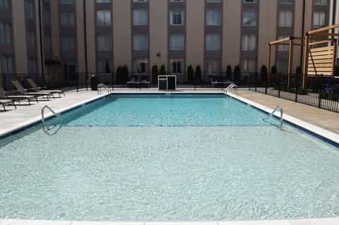 Hotel pool with shallow and deep sections, lounge chairs, and multi-story building backdrop