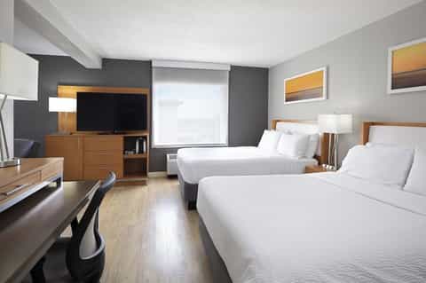 Hotel room with two queen beds, TV, desk, and modern furnishings in neutral tones