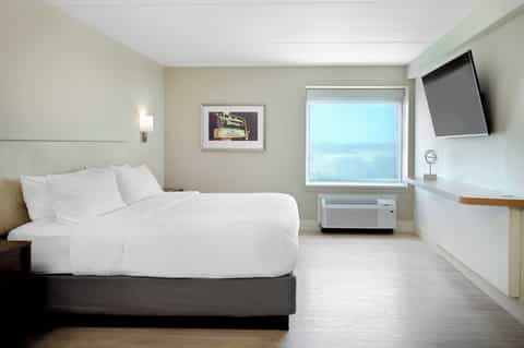 Spacious hotel room with single bed, TV, window with light control, and minimalist décor