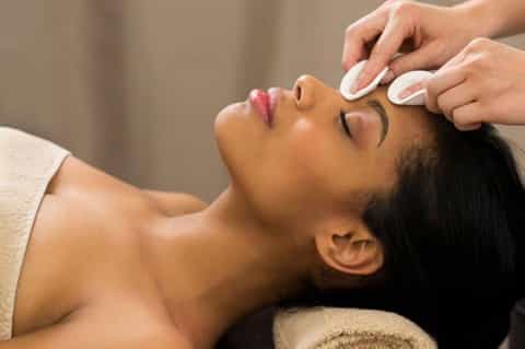 Spa therapist applying facial treatment to woman's face with white cloth