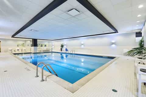 Indoor lap pool with bright blue water, white ceiling, railings, and clean minimalist spa facility design
