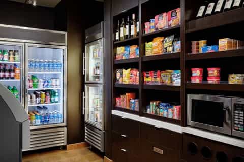 Hotel convenience store with refrigerated beverages, snacks on shelves, and microwave