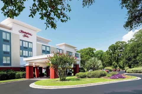 Hampton Inn hotel exterior with white facade, red accents, and landscaped entrance